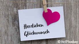Zettel mit Herz hängt an einer Leine. Auf dem Zettel steht "Herzlichen Glückwunsch".
