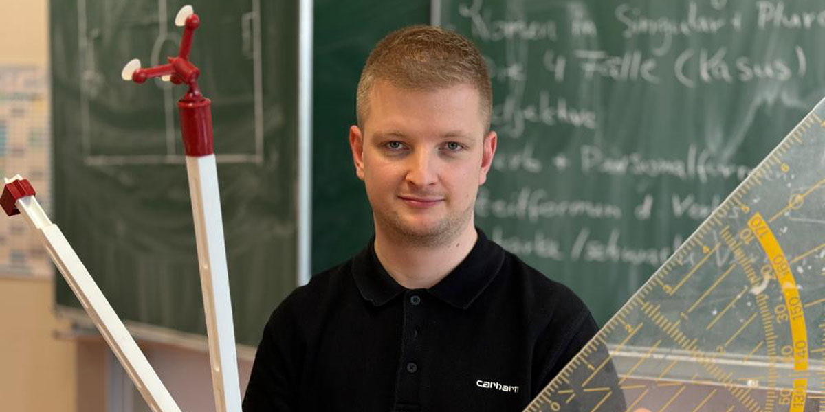 hr-Reporter Simon Rustler mit großem Geodreieck und Zirkel vor einer Tafel