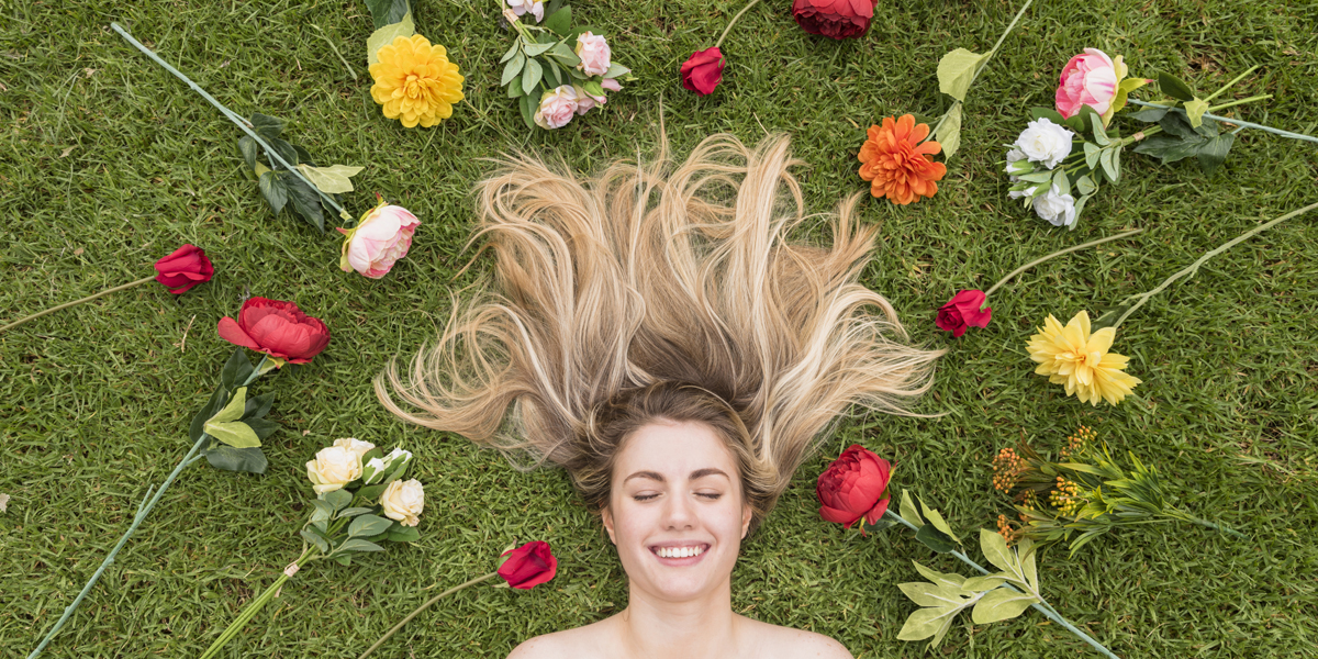 Eine junge Frau liegt im Gras umgeben von Blumen.