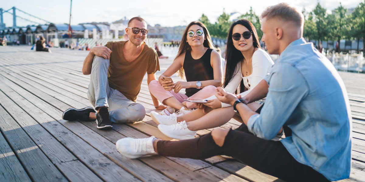 vier junge Leute sitzen im Sommer auf einem Holzsteg 