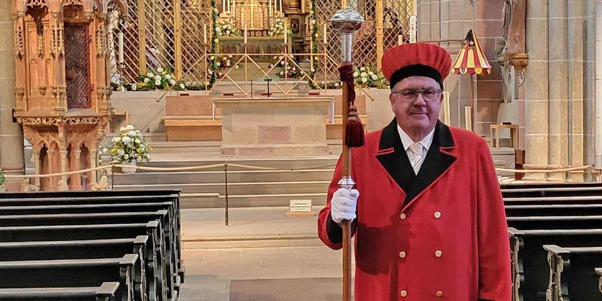 Domschweizer Thomas Drößler mit Stab und Dienstmontur  im Dom zu Fritzlar: roter Mantel, rote Haube, weiße Handschuhe