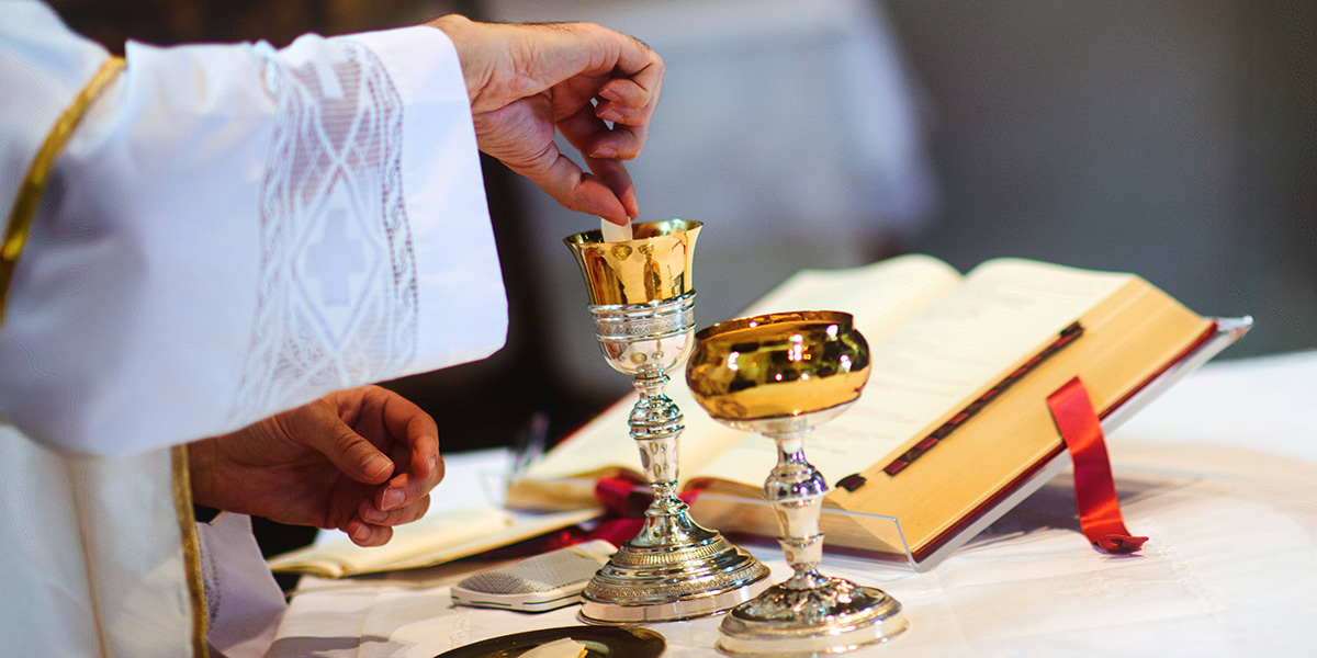 Priester taucht Hostie in einen Weinkrug auf einem Altar