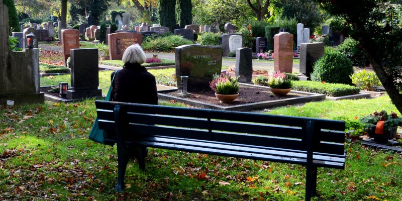 Rückansicht einer Frau auf einer Friedhofsbank