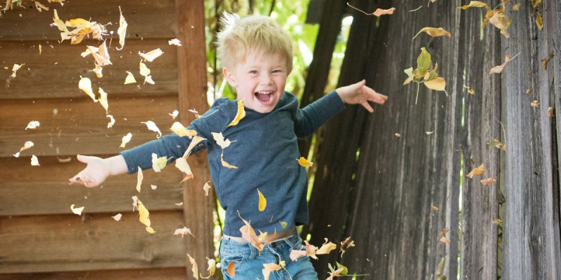 Ein Junge wirbelt Herbstlaub auf und lacht
