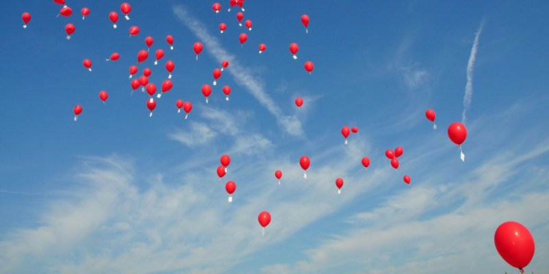 rote Luftballons steigen in einen blauen Himmel auf