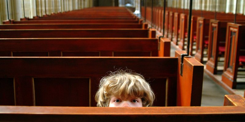 Junge in einer leeren Kirche lugt über eine Kirchenbank